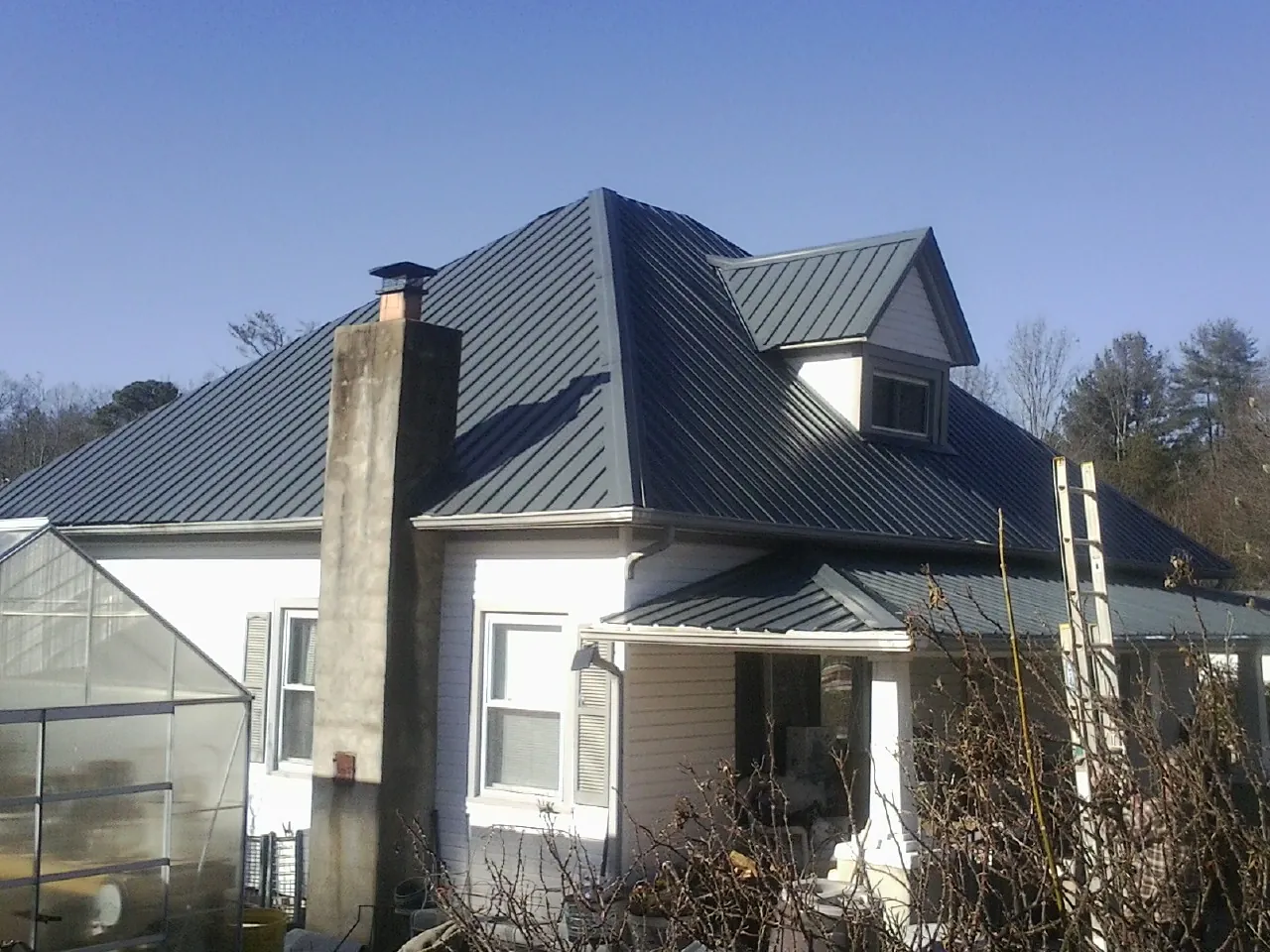 Dark blue standing seam metal roof on a white farmhouse with dormer — Slate & Tile Roof Repair by Roofing Brothers in Crookston