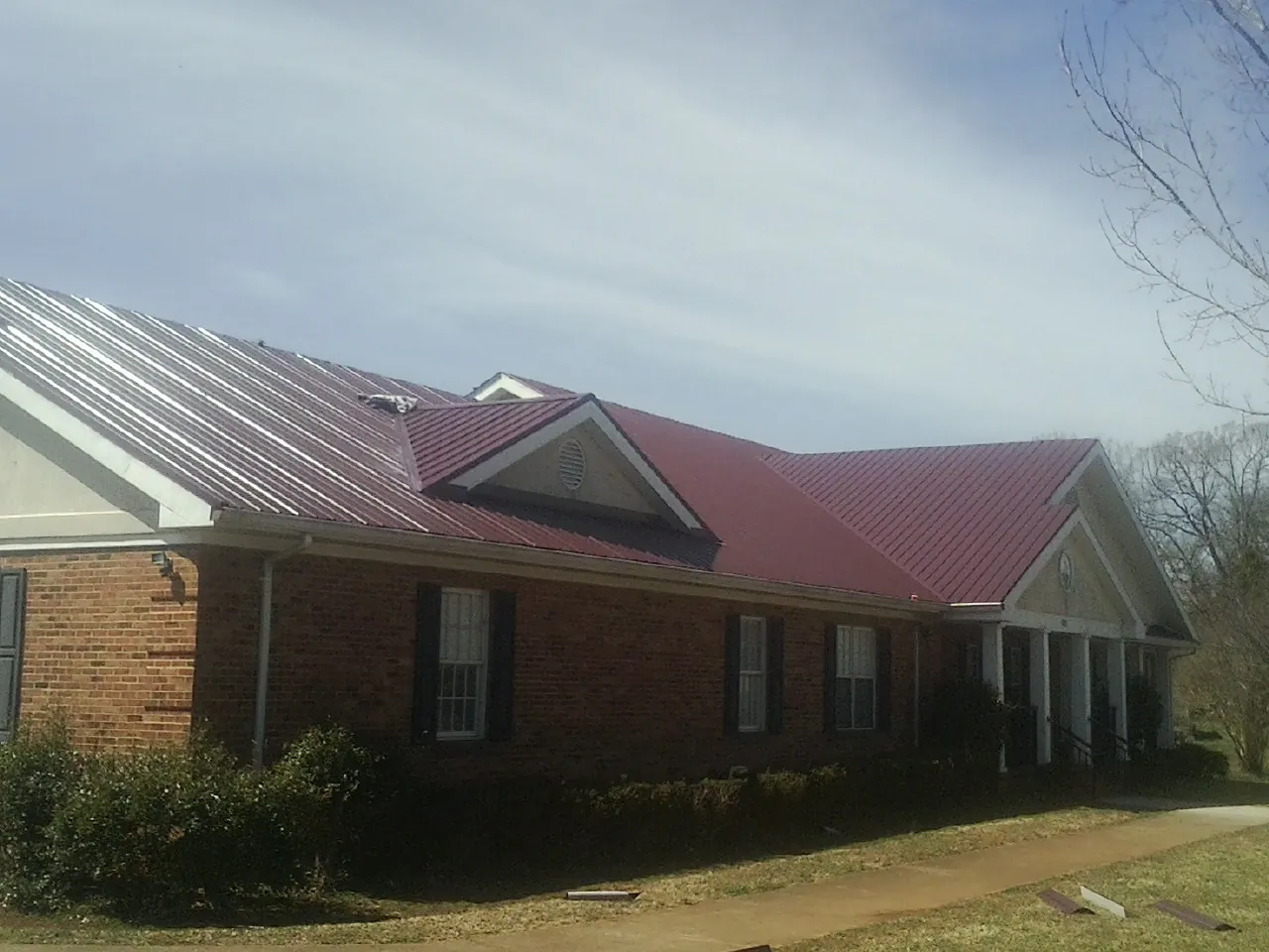 Red metal roof with gabled entries on a long brick building, from a Hail Damage Roof Repair job in Crookston