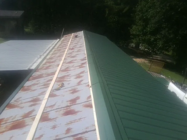 Old rusted panels beside newly installed green metal roofing — Wind Damage Roof Repair by Roofing Brothers in Crookston