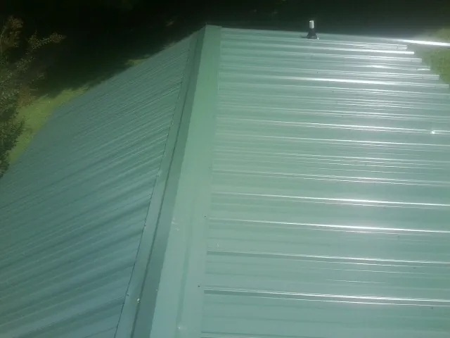 New green metal panels meeting at the ridge of a roof — Flat Roof Repair work by our crew in Crookston