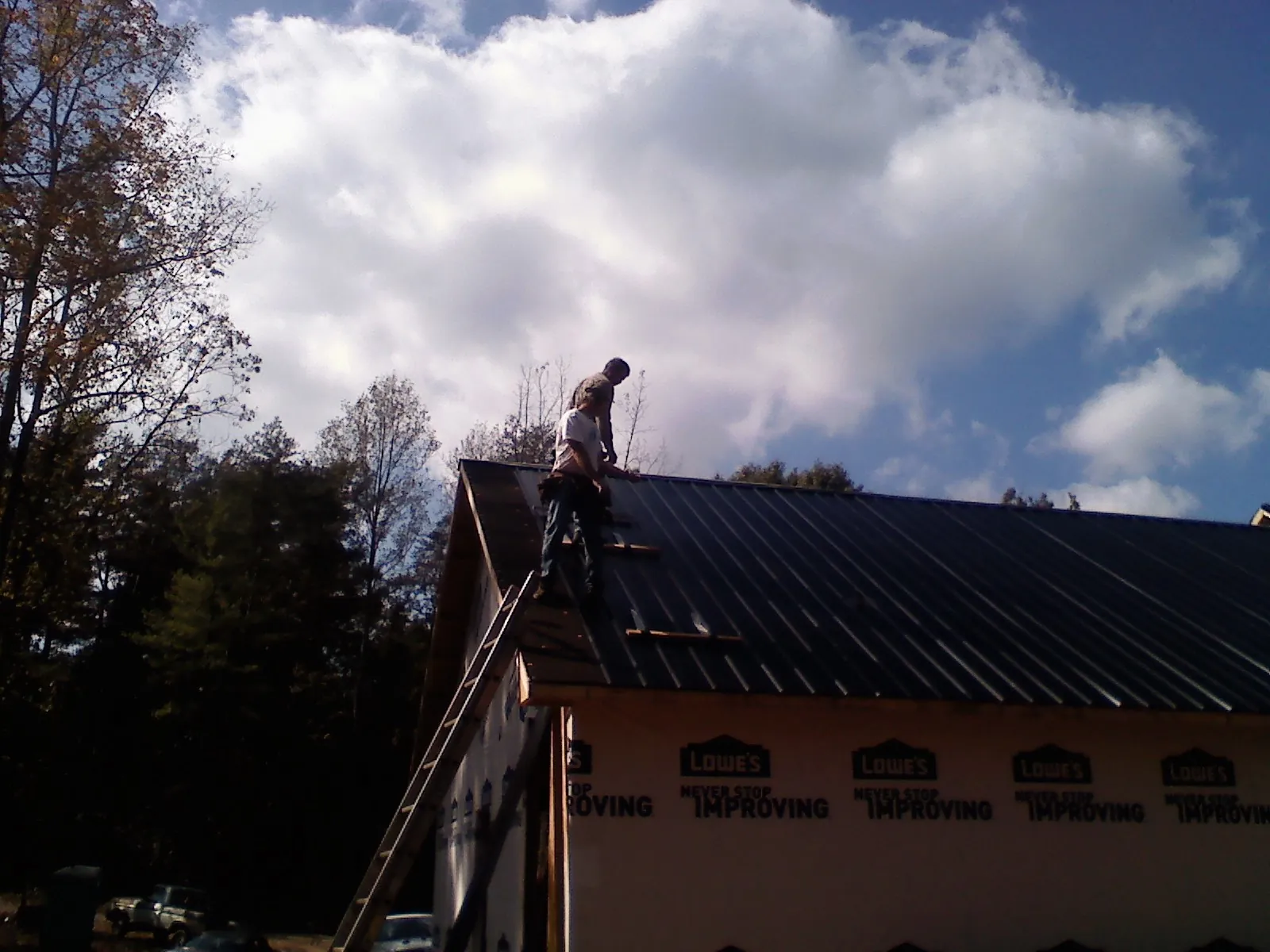 Roofer fastening dark metal panels high against a cloudy sky, from a Roof Inspection job in Crookston