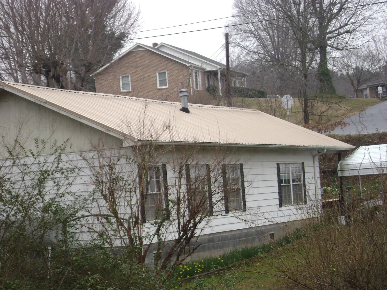 Tan metal roof on a white sided house set into a hillside — Commercial Roofing by Roofing Brothers in Crookston