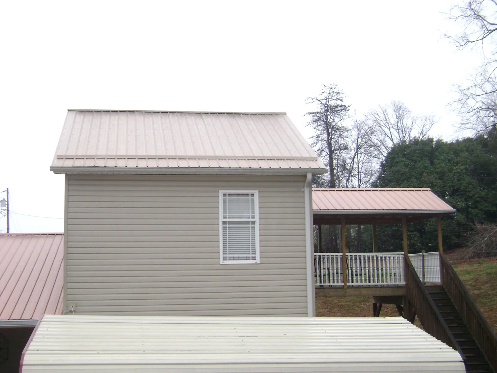 Tan metal roofs on a two story addition and attached porch, from a Roof Replacement job in Crookston